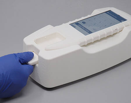 A photograph of a gloved hand feeding a card into a medical device